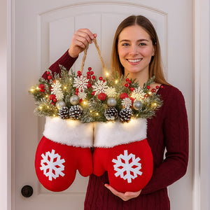 Decorative red mittens with white snowflakes holding a festive wreath on a white door.