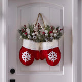 Decorative red mittens with white snowflakes holding a festive wreath on a white door.