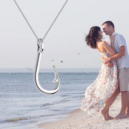Silver fish hook pendant with a couple embracing on a beach.