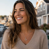 Woman wearing a beige sweater with a necklace featuring a fish hook pendant, standing outdoors.